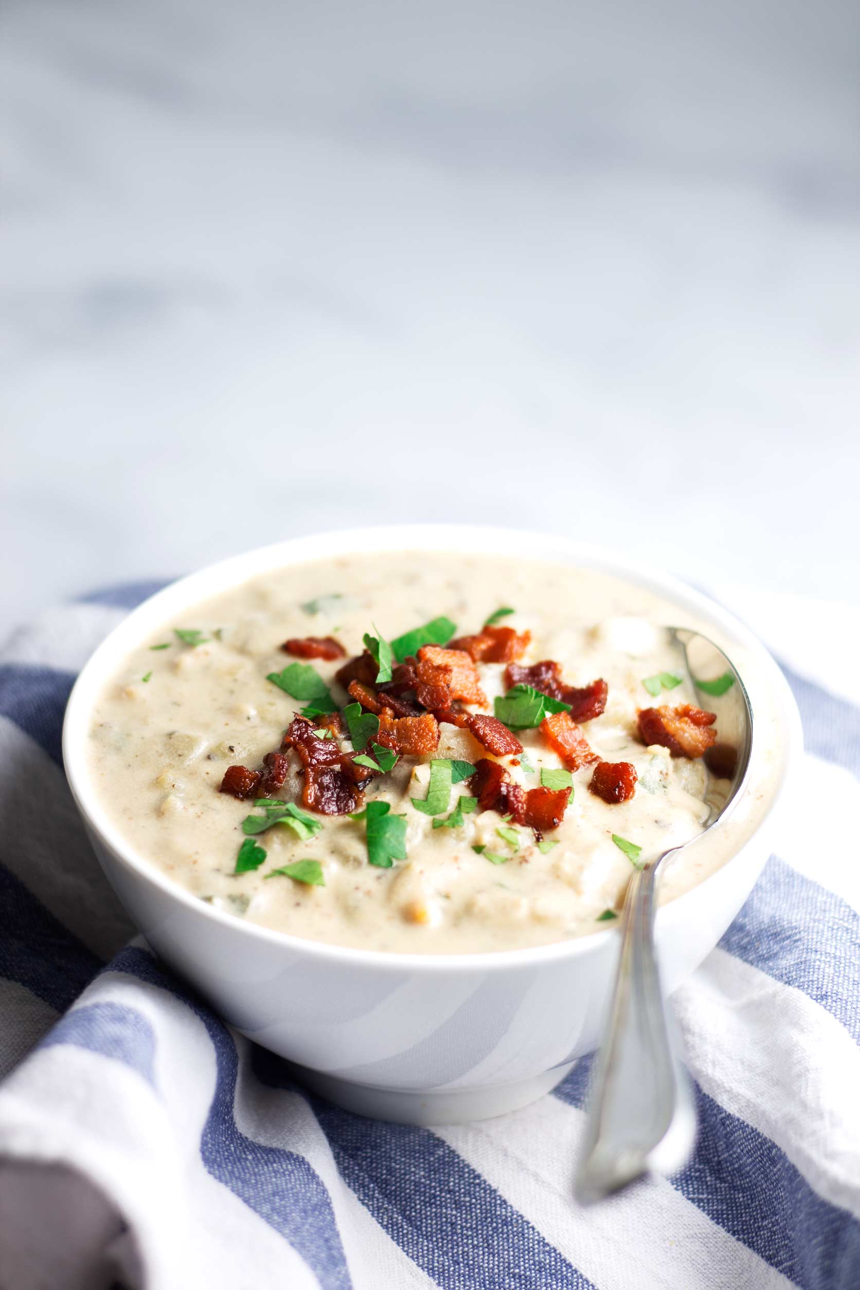 Dairy Free Clam Chowder in white bowl on top of blue and white striped kitchen towel