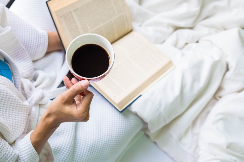woman on bed with book and cup of coffee 