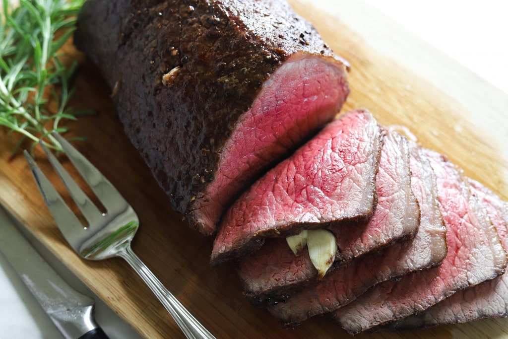 roast beef sliced on cutting board with rosemary and serving fork, how to cook melt in the mouth roast beef