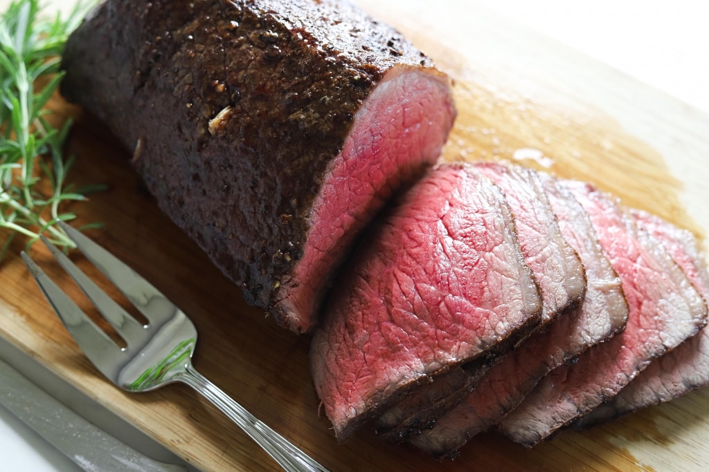 roast beef sliced on cutting board with rosemary and serving fork, how to cook melt in the mouth roast beef