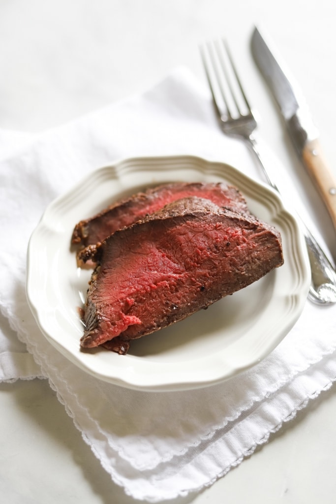 slices of roast beef on plate with fork and knife and white napkin