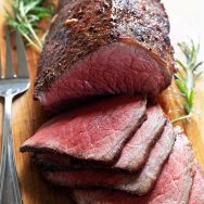 roast beef sliced on cutting board with rosemary and serving fork