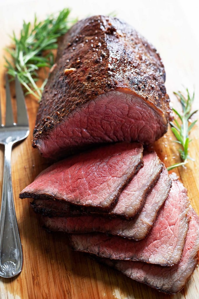 roast beef sliced on cutting board with rosemary and serving fork, how to cook melt in the mouth roast beef