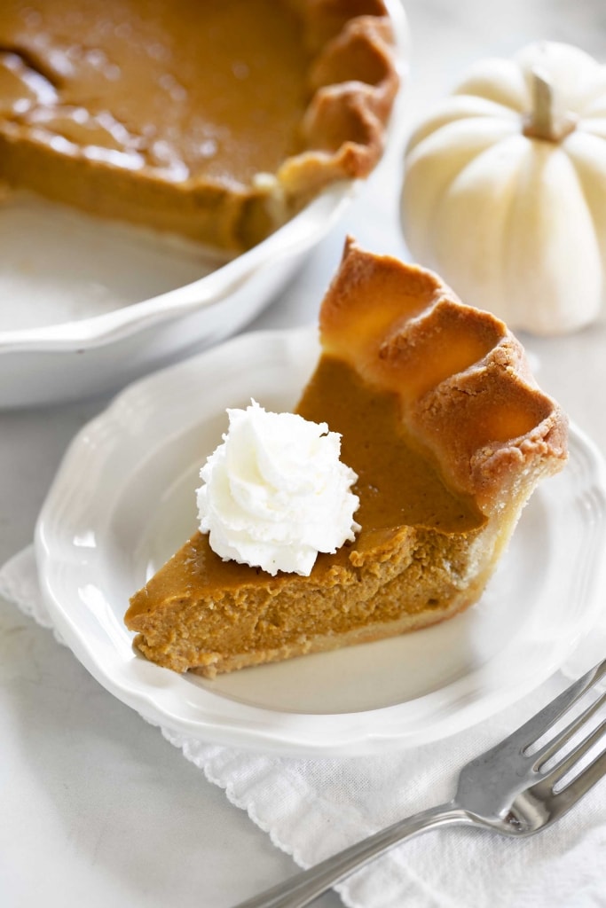 pumpkin pie slice on white plate with whipped cream