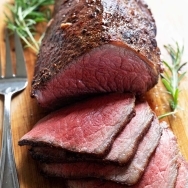 roast beef sliced on cutting board with rosemary garnish
