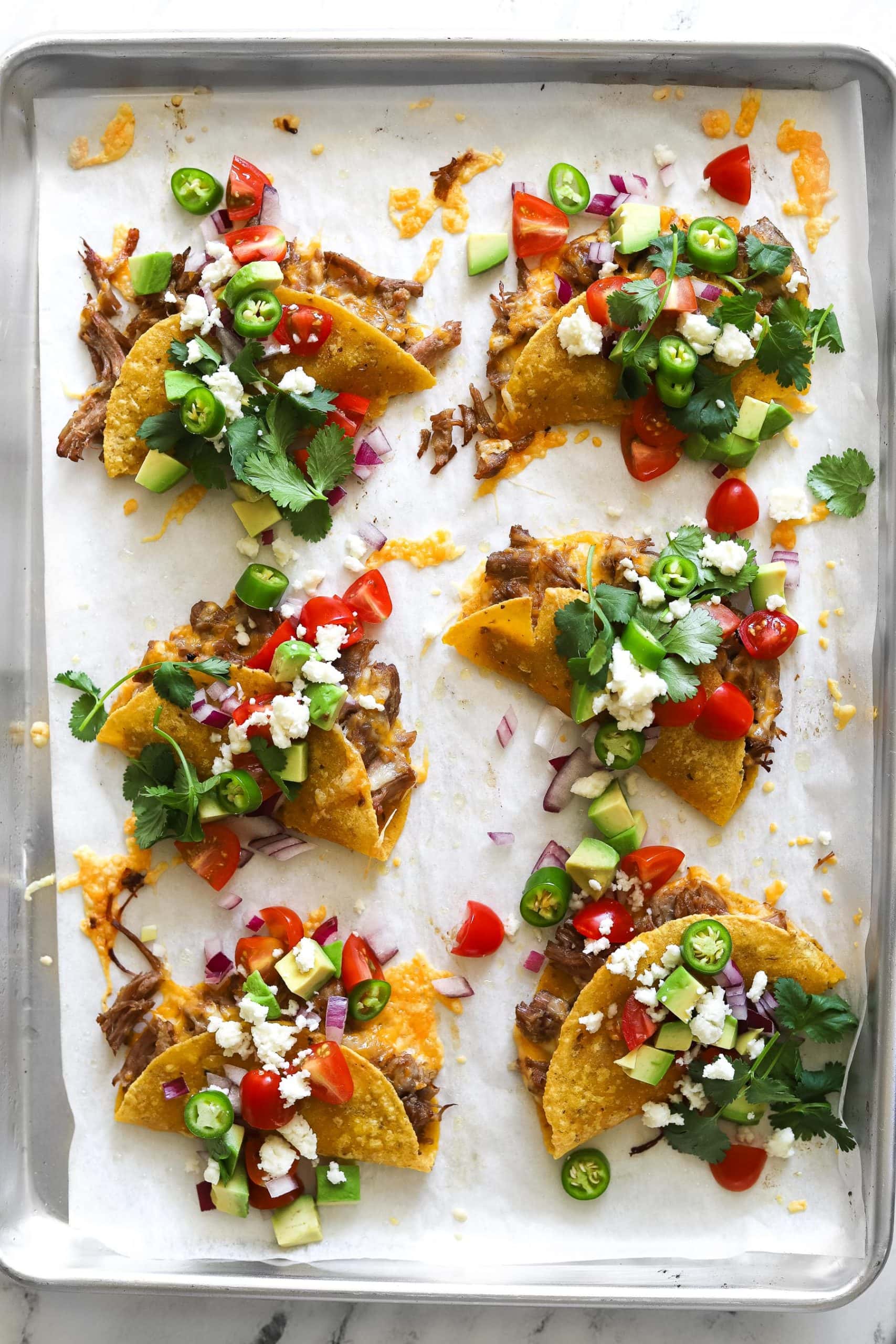 Crispy baked carnitas tacos on sheet pan with toppings