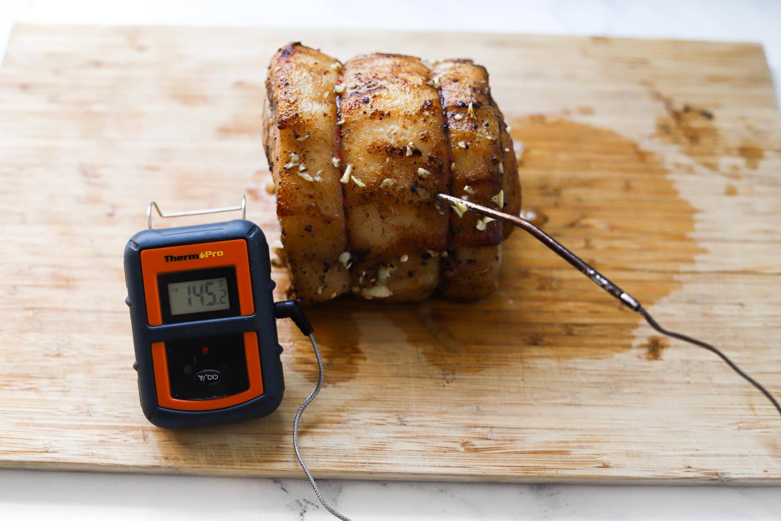 pork loin cooked and resting on cutting board with thermometer showing 145 degrees F