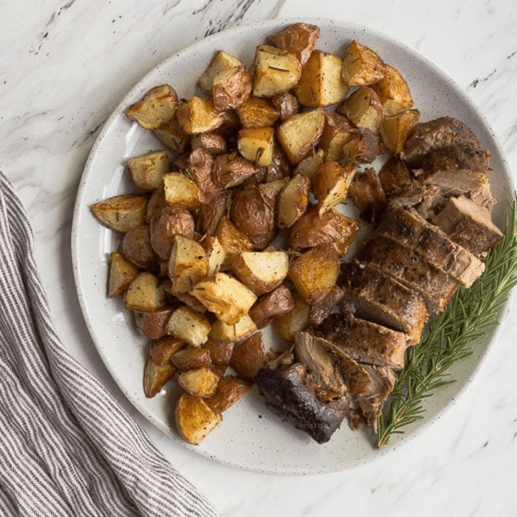Pork loin with roasted potatoes on a white plate.