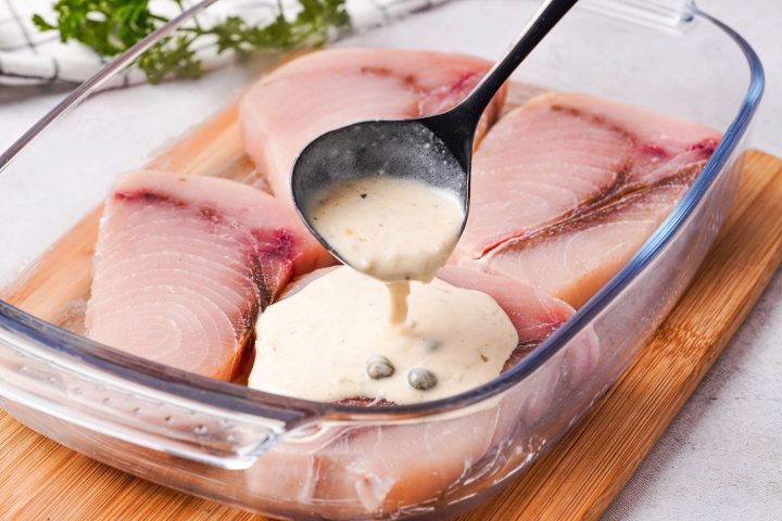 pouring cream sauce over raw swordfish steaks in baking dish