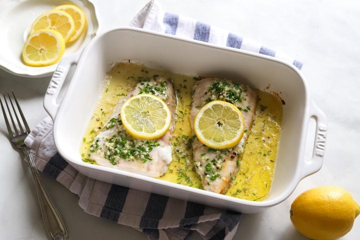 two halibut fillets with lemon on top in baking dish