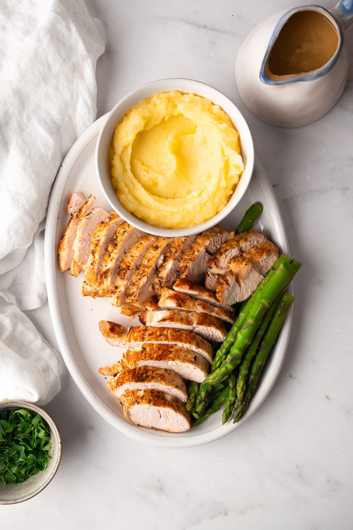 turkey sliced on white oval dish with mashed potatoes and asparagus