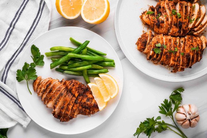 blackened chicken breast sliced on plate with green beans and lemon