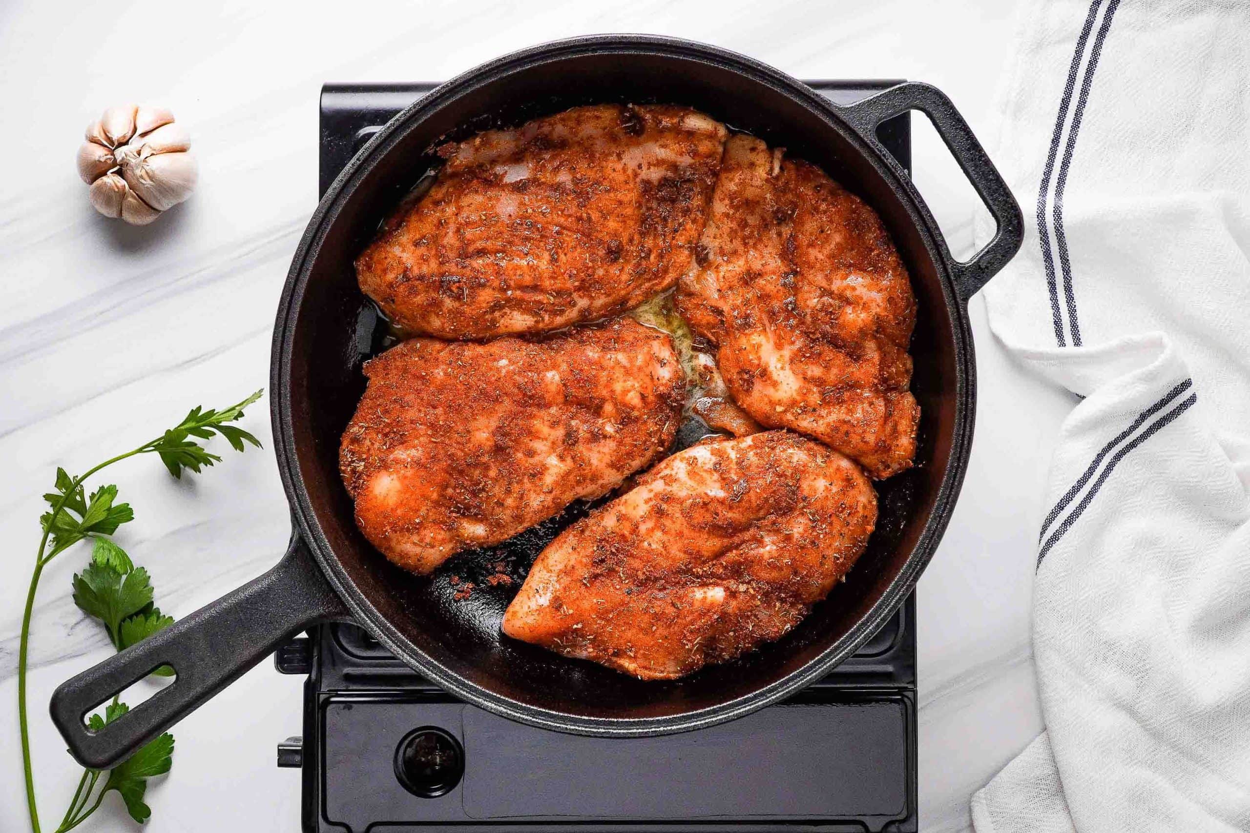 seasoned chicken breasts in skillet beginning to cook