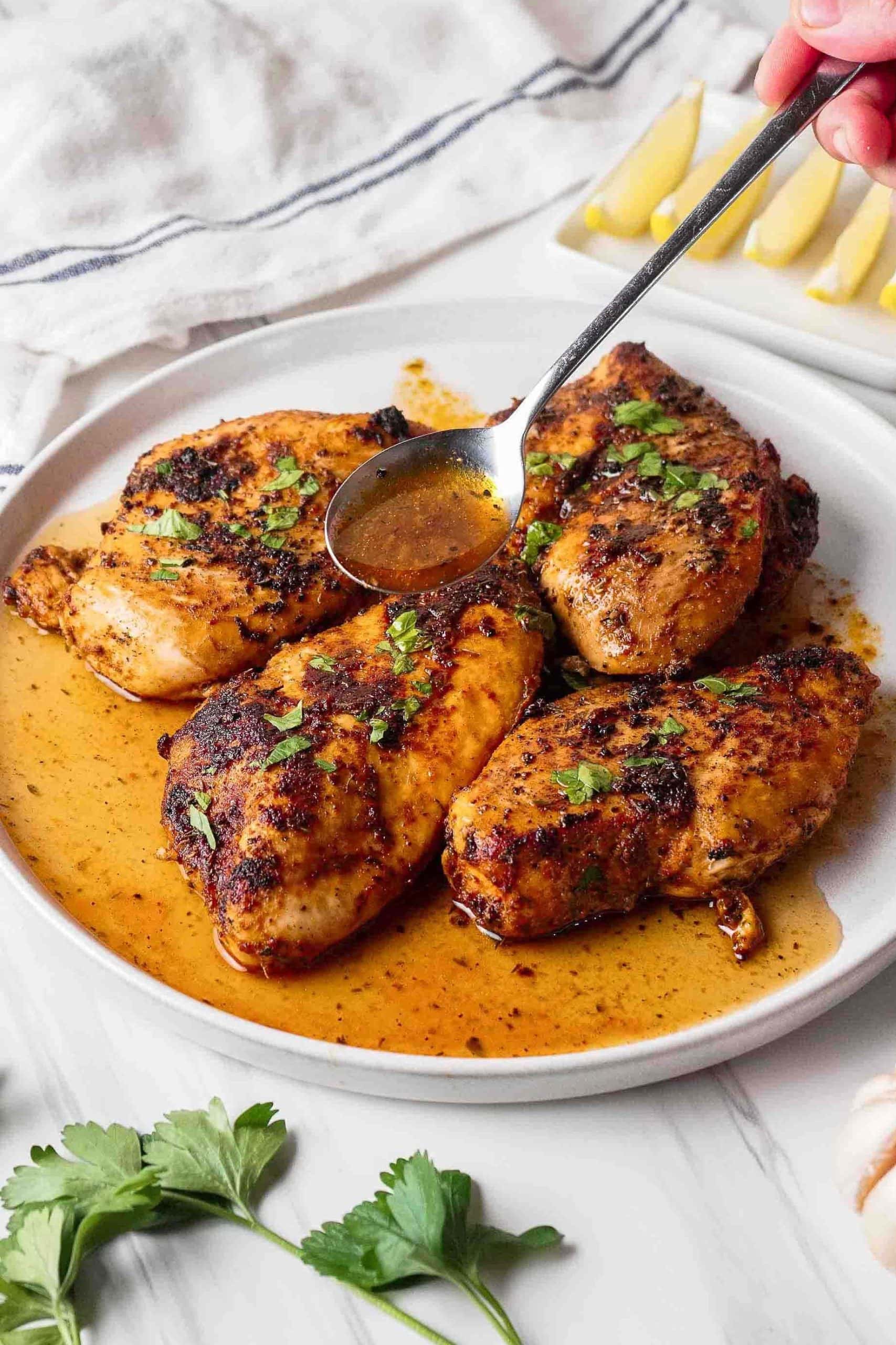 chicken breasts on white plate spooning on butter mixture after cooking