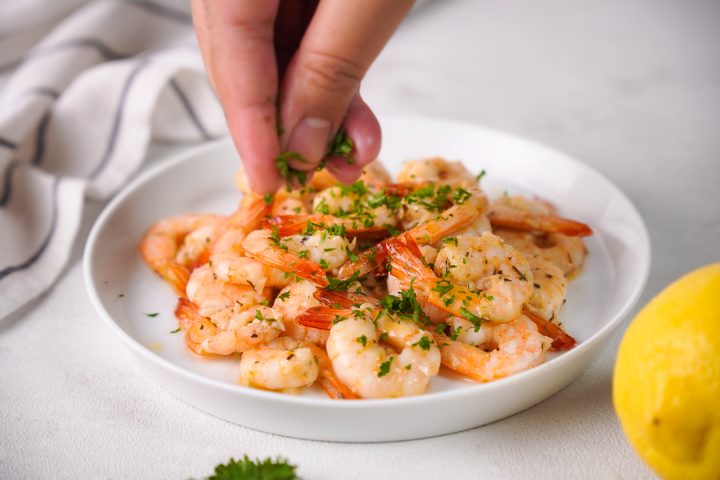 sprinkling chopped parsley on shrimp on white plate with white background