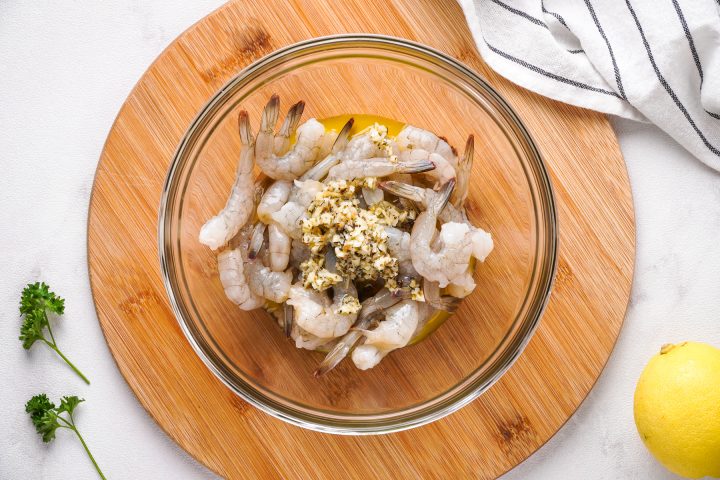 raw shrimp in bowl with garlic butter poured on top before mixing