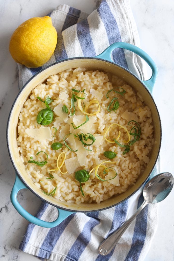 lemony risotto in blue pot with striped dish towel and garnish of basil and lemon peel curls